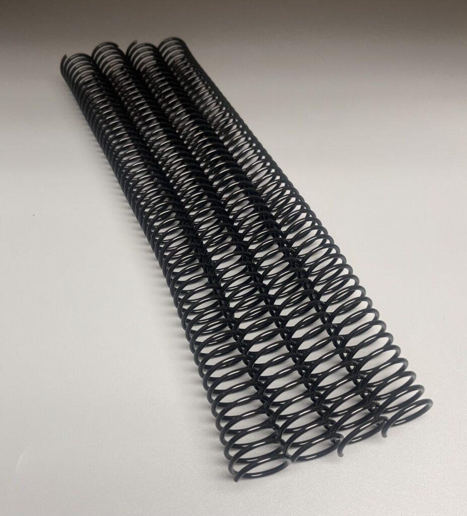 Three black metal coil bindings are lined up on a light gray surface.