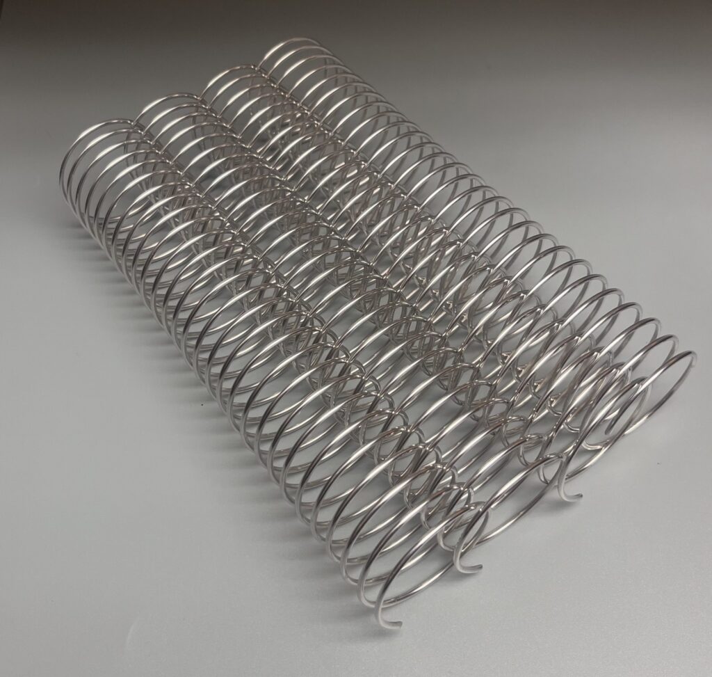 Four metallic coil springs are aligned parallel on a smooth, gray surface.