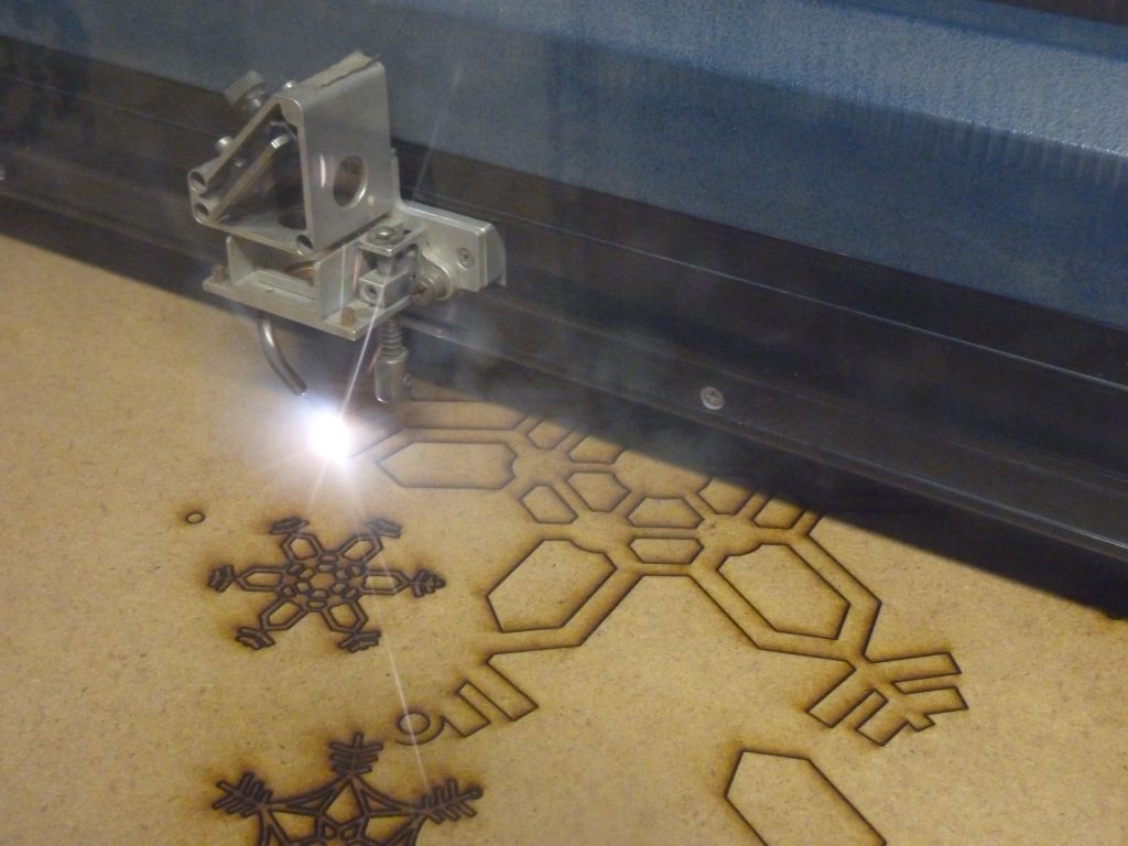 A laser cutter, using Laser Engraving in Torrance, engraves intricate snowflake shapes into a sheet of wood.