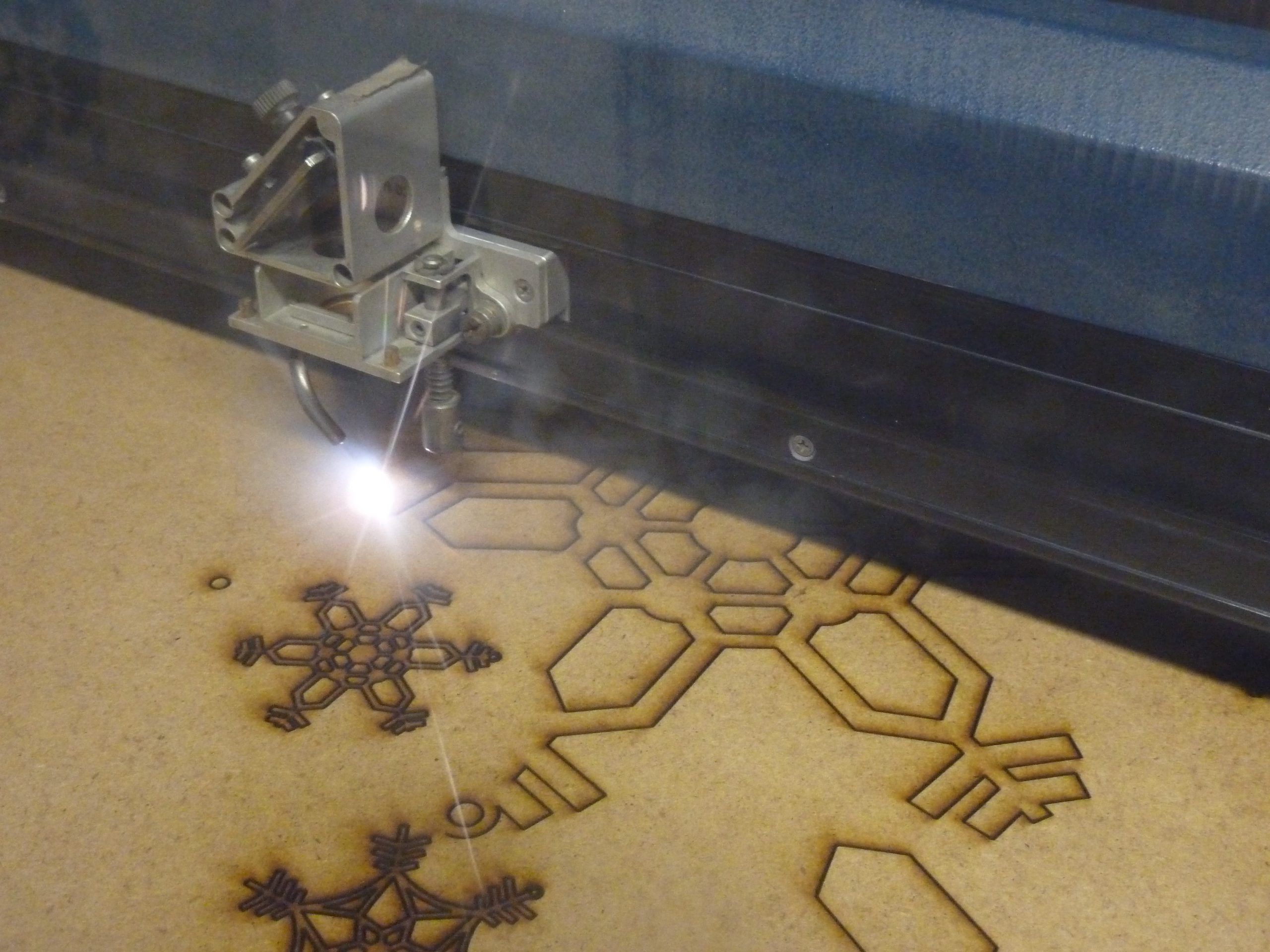 A laser cutter, using Laser Engraving in Torrance, engraves intricate snowflake shapes into a sheet of wood.