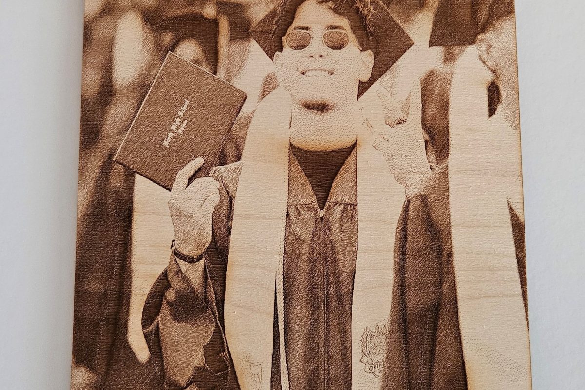 A graduate in cap and gown smiles, holding a diploma with a peace sign at a graduation ceremony, celebrating achievements that could be commemorated with personalized gifts from Laser Engraving Services.