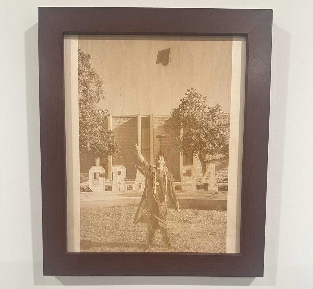 Pic-frame Framed photo of a graduate tossing a cap in the air, with "GRAD" letters and trees in the background. Personalize your moment with our Laser Engraving Services, perfect for commemorating this special achievement.