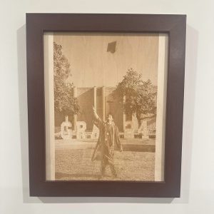 Laser-Engraved Portrait with Frame featuring a graduate tossing a cap outdoors, with large "GRAD" letters and trees in the background.