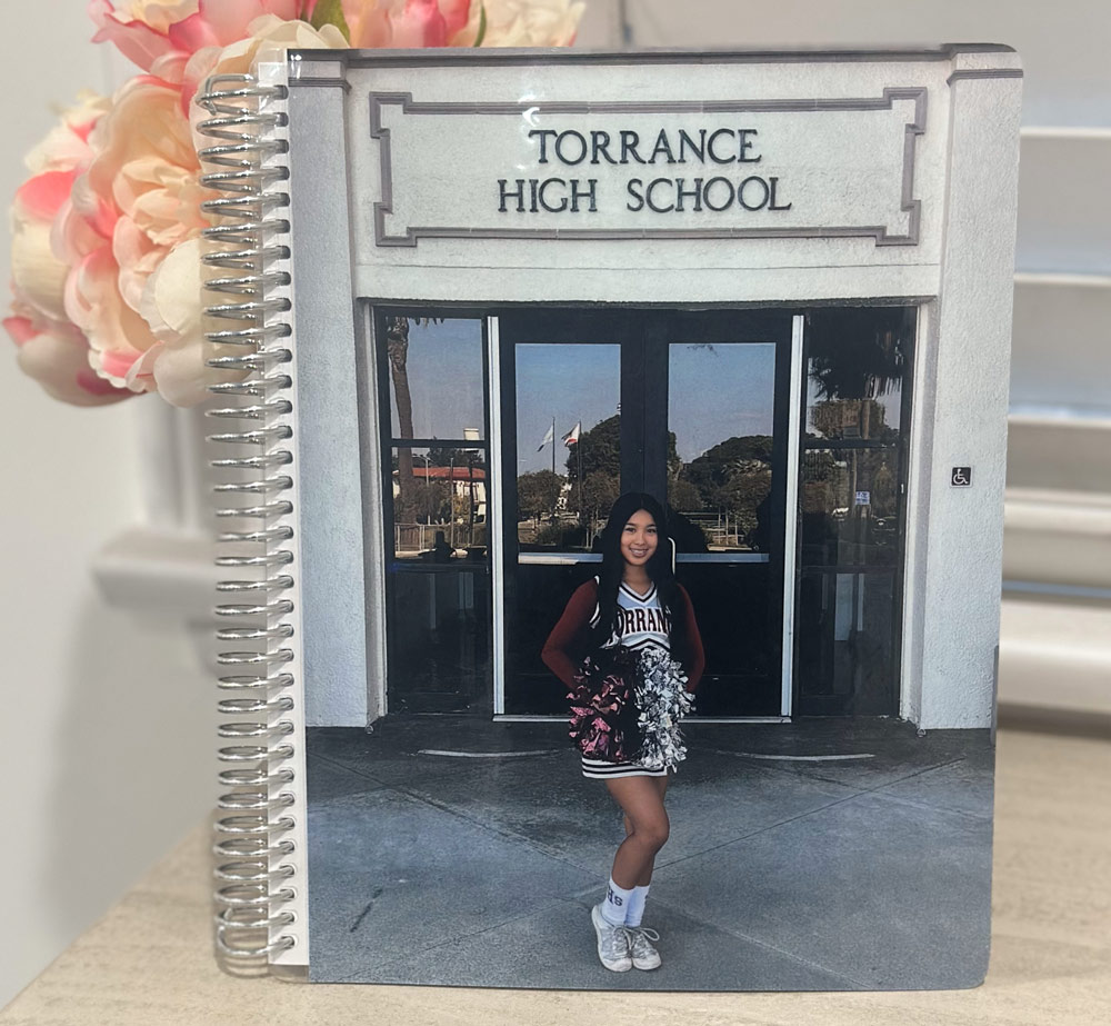 notebook A smiling cheerleader stands in front of the entrance to Torrance High School, holding pom-poms personalized with Laser Engraving Services.