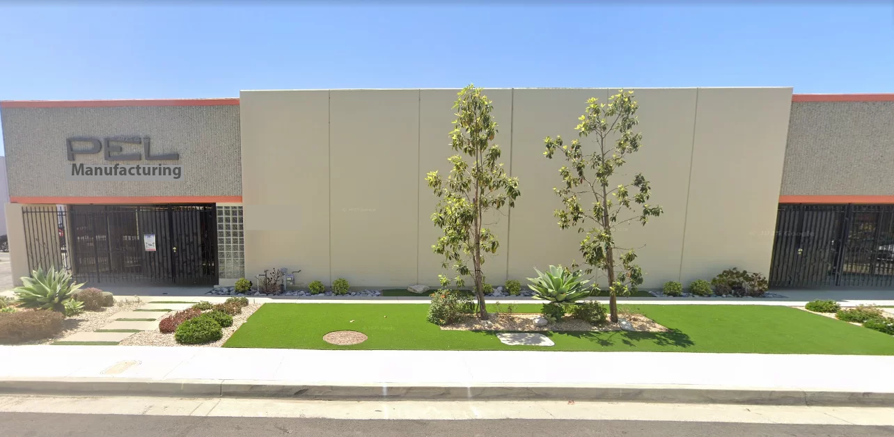Front view of a beige industrial building labeled "PEL Manufacturing" with small trees and landscaping.