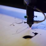 A laser cutter precisely engraving colorful spiral coils onto a sheet of wood, creating an intricate and vibrant design.
