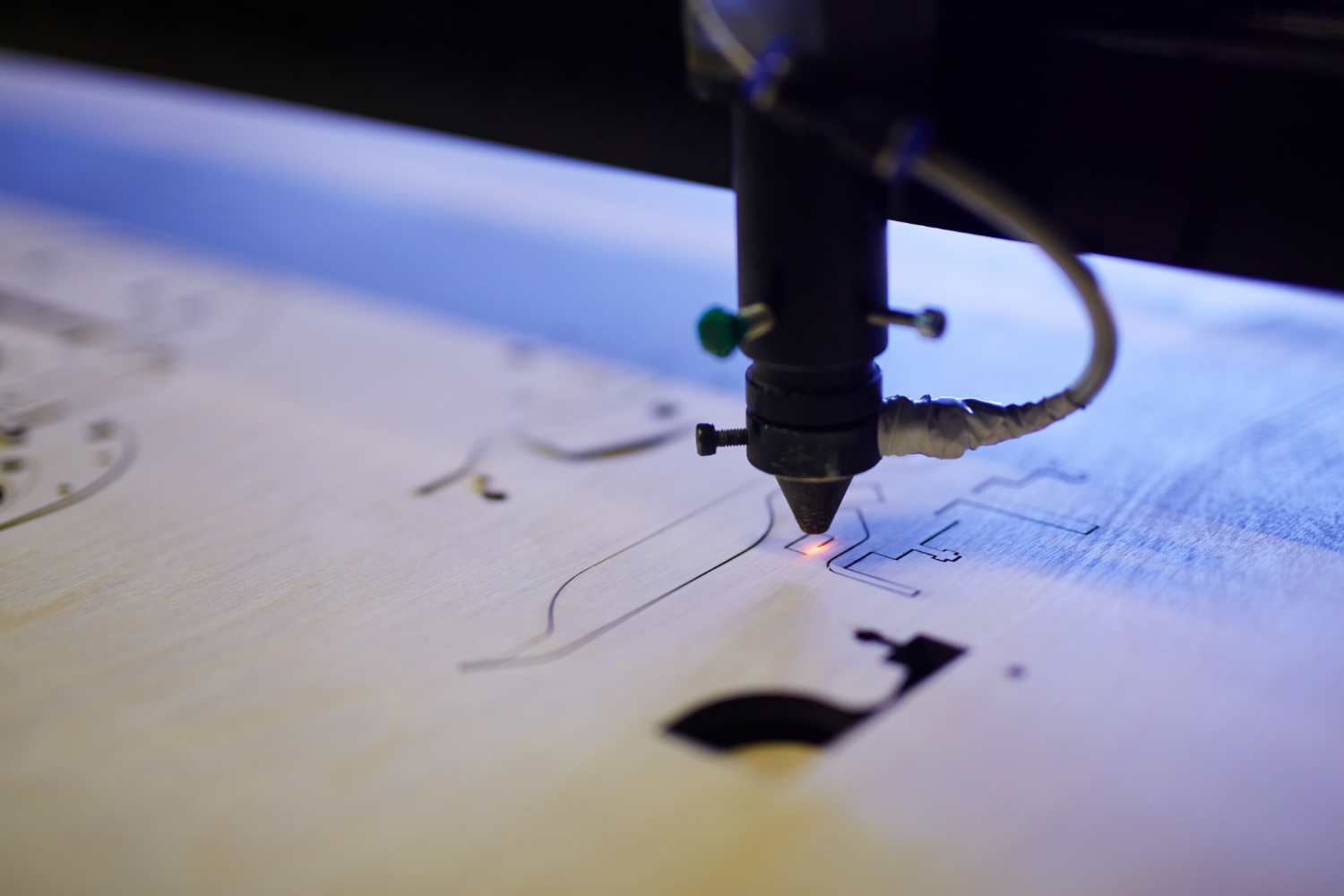 A laser cutter precisely engraving colorful spiral coils onto a sheet of wood, creating an intricate and vibrant design.