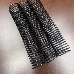 A 1+3/4" x10" #3wo Black Plastic Spiral (1 Piece) rests on a wooden surface.