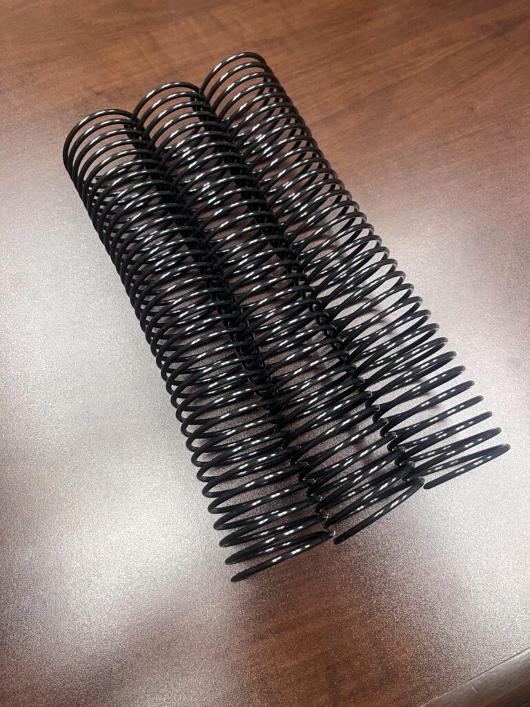 A 1+3/4" x10" #3wo Black Plastic Spiral (1 Piece) rests on a wooden surface.