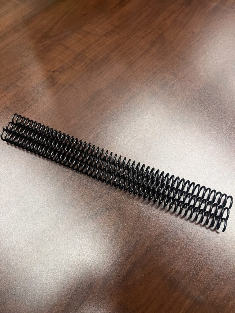 A set of 7/16" x12" #4 Black Spiral Plastic binding spines (3 pieces) placed on a wooden surface.