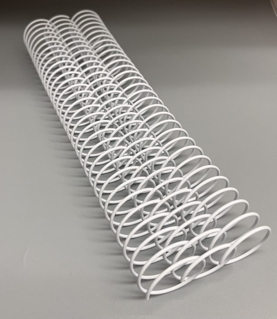 A 1+3/8" x 12" #2.5 White Spiral Wire (1 Piece) is displayed in a row on a gray surface.