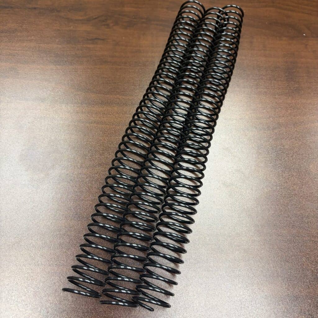 Three 15/16" x 12" #3.5 black plastic spirals are placed side by side on a brown wooden surface.