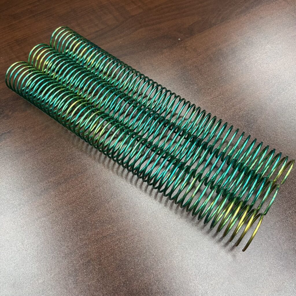 A 1+1/4" x12" #4 Green Burst Solid Coil is placed on a brown wooden surface.