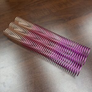 A 1+1/4" x12" #4 Petunia Solid Spiral binding coil is displayed on a wooden surface.