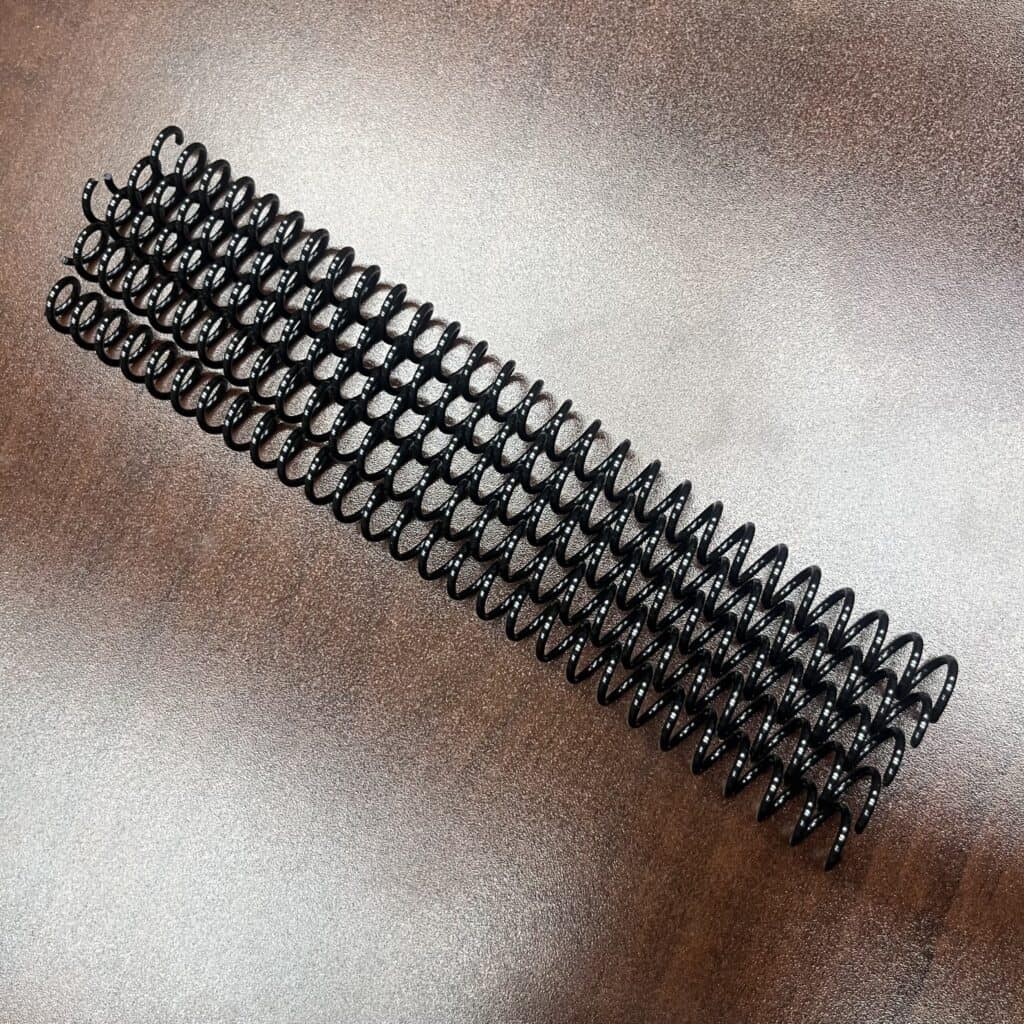 Five 5/16" x 7" #4 black spiral plastic binding coils (set of 5 pieces) are lined up on a brown wooden surface.
