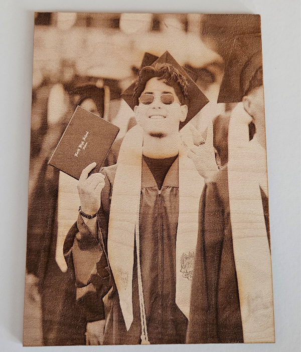 Person in graduation attire smiling and holding a diploma, wearing sunglasses and a cap.