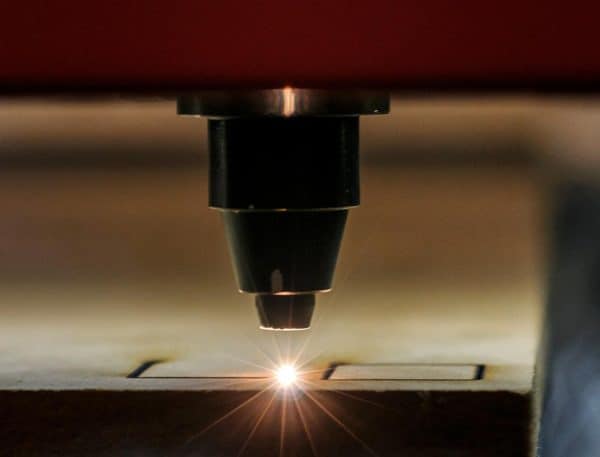 Close-up of a laser cutter beam cutting shapes into a flat sheet of material, with a bright spark visible.