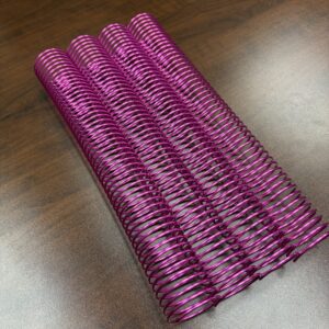 Four 1+1/2″ x 12″ #4 Neon Pink Solid Spiral binding coils are lying side by side on a wooden surface.