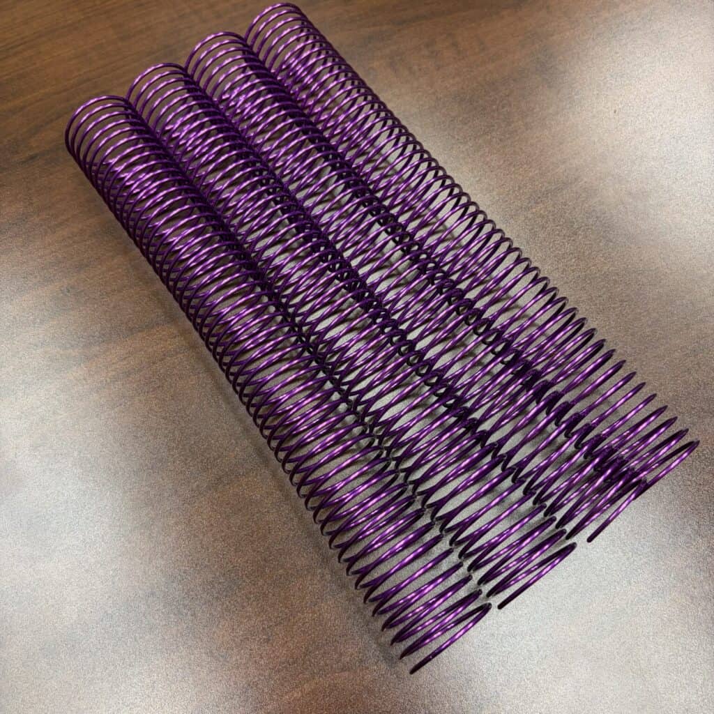 A single 1+1/2″ x12″ #4 Violet Solid Spiral Aluminum binding coil is placed on a wooden surface.