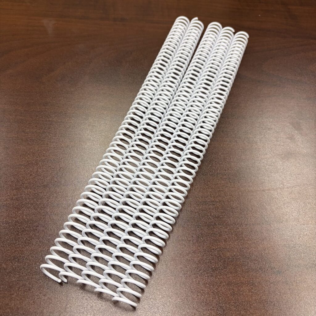 Four 1/2″ x 12″ #4 White Spiral Plastic binding spines are laid parallel on a brown wooden surface.