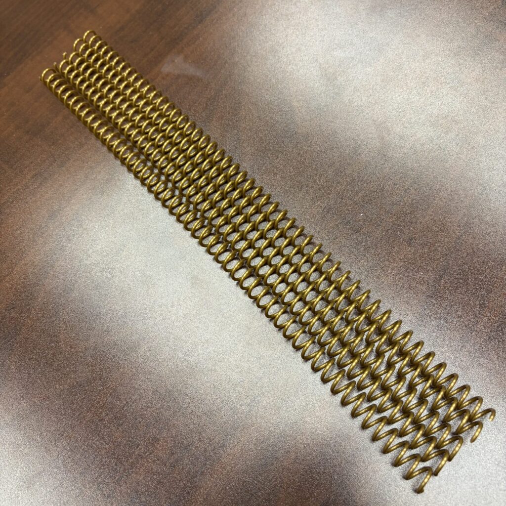 Five 5/16″ x12″ #4 Gold Plastic Spiral Coil pieces laid side by side.
