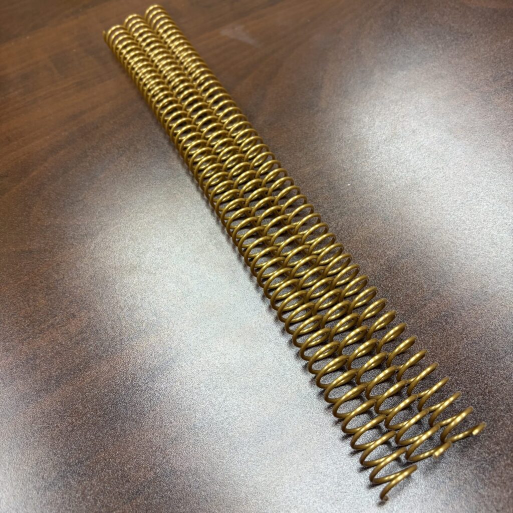 A long, gold 1/2″ x12″ #4 Gold Spiral Plastic spiral binding coil.