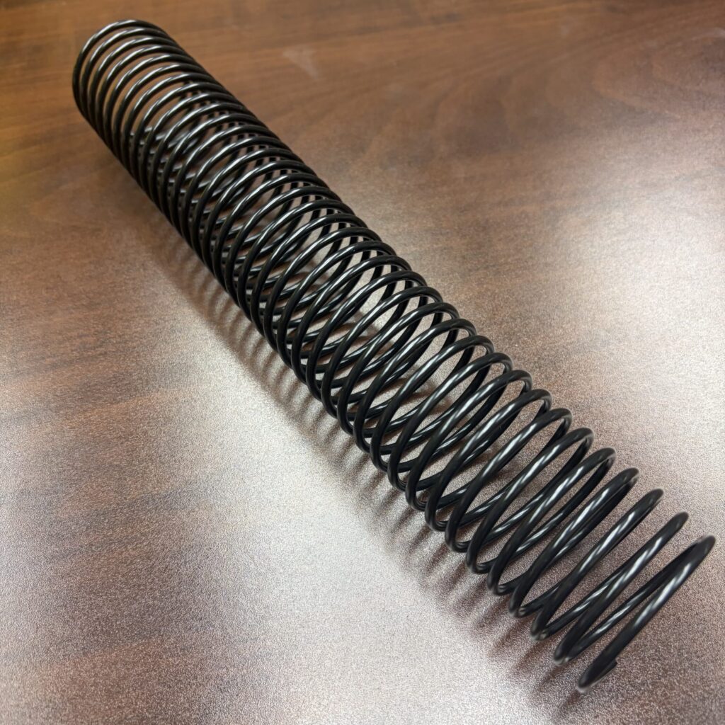 A black 1+13/16″ x12″ #3wo Black Spiral Plastic coil on a wooden surface.