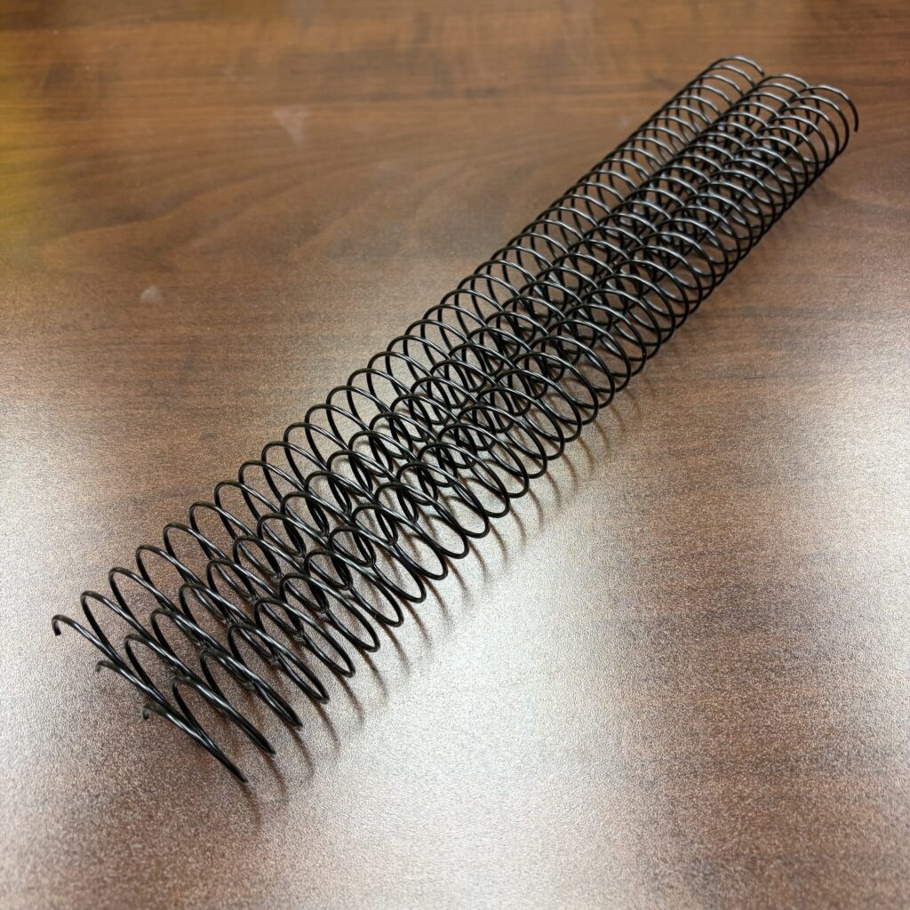 A 1″ x12″ #3wo Black Spiral Wirem metal coil on a wooden surface.